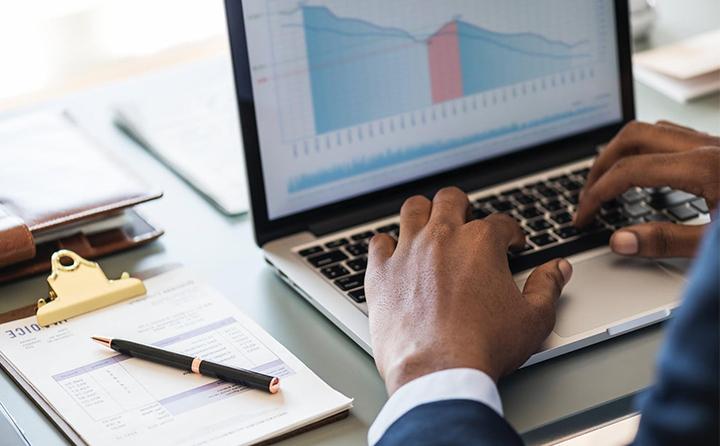 Photo of person typing on a laptop with a business chart on it